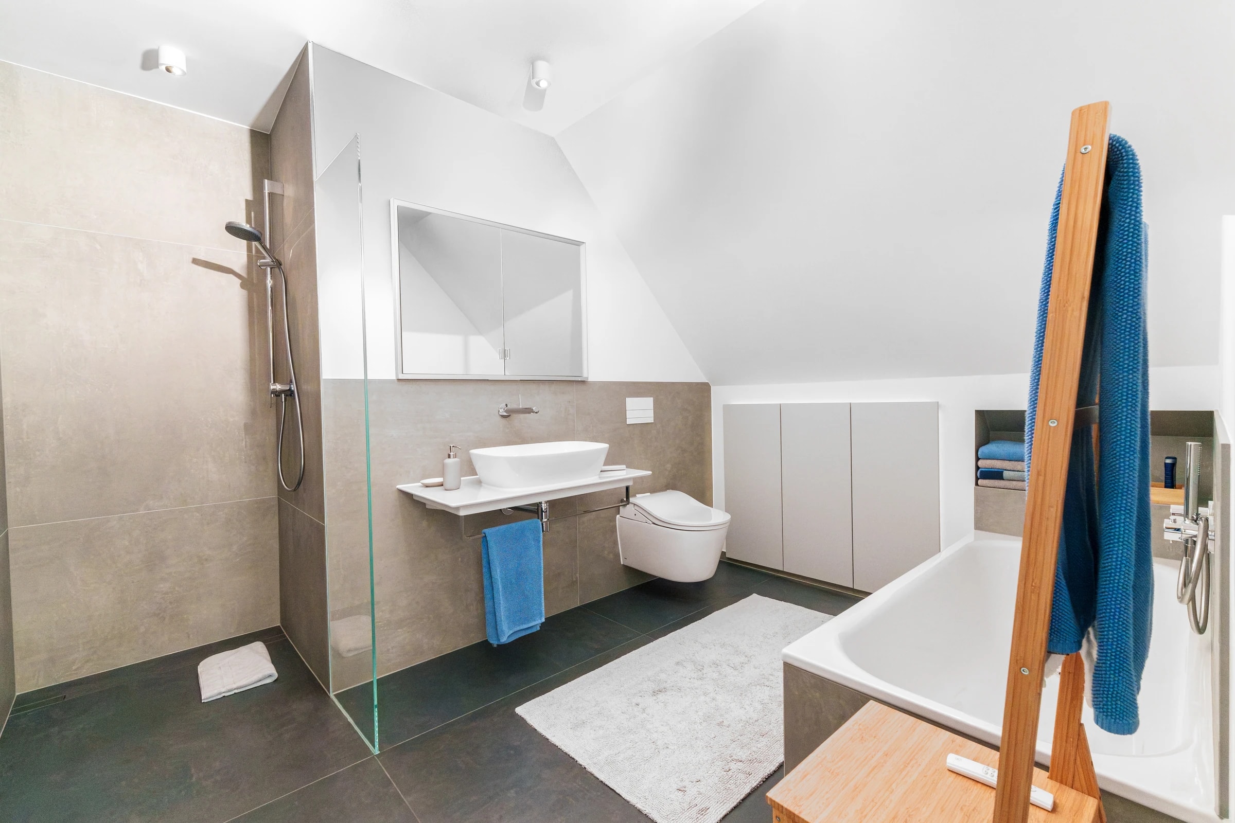Helles Dachgeschossbad mit bodengleicher Dusche, Waschtisch, Wanne und blauen Handtüchern